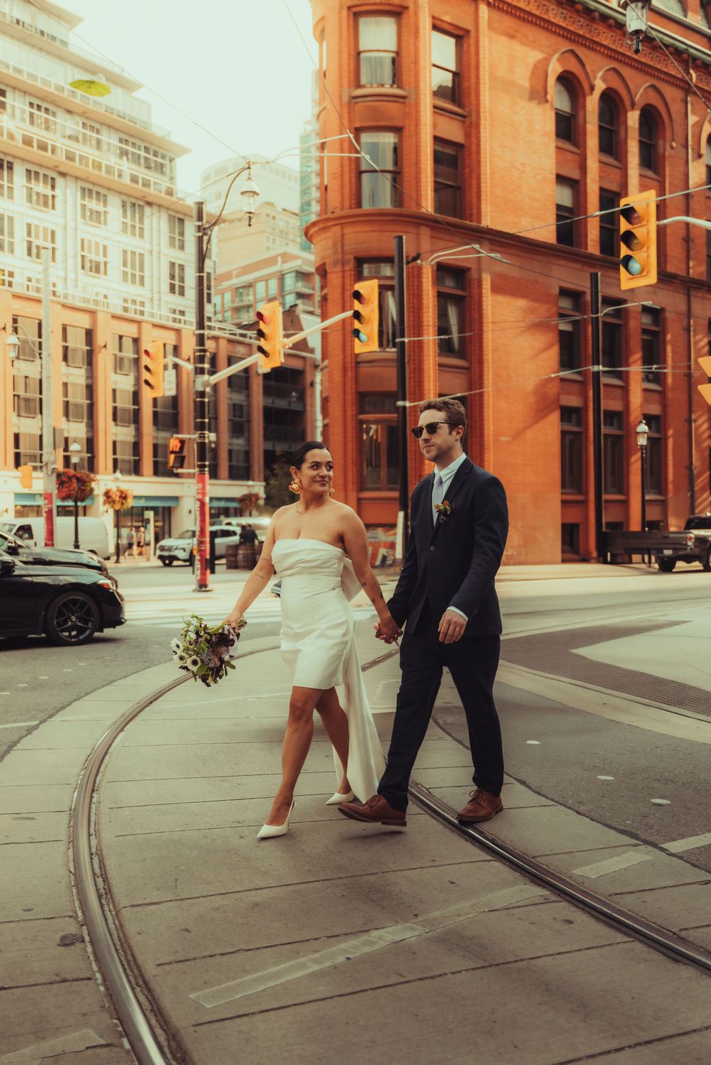 Golden hour photo of a bride and groom walking in a cross walk in front Gooderham Building