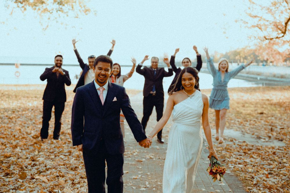 golden hour photo of bride and groom while she is holding a bouquet of flowers and walking towards the camera and the family is behind them