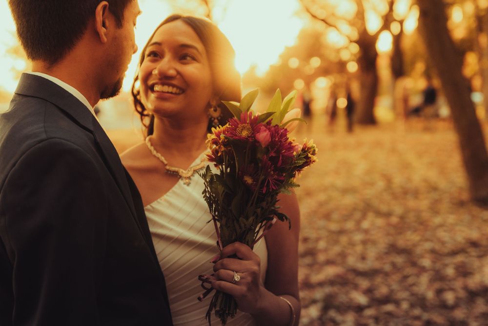 golden hour photo of bride and groom while she is holding a bouquet of flowers as the sun is behind them