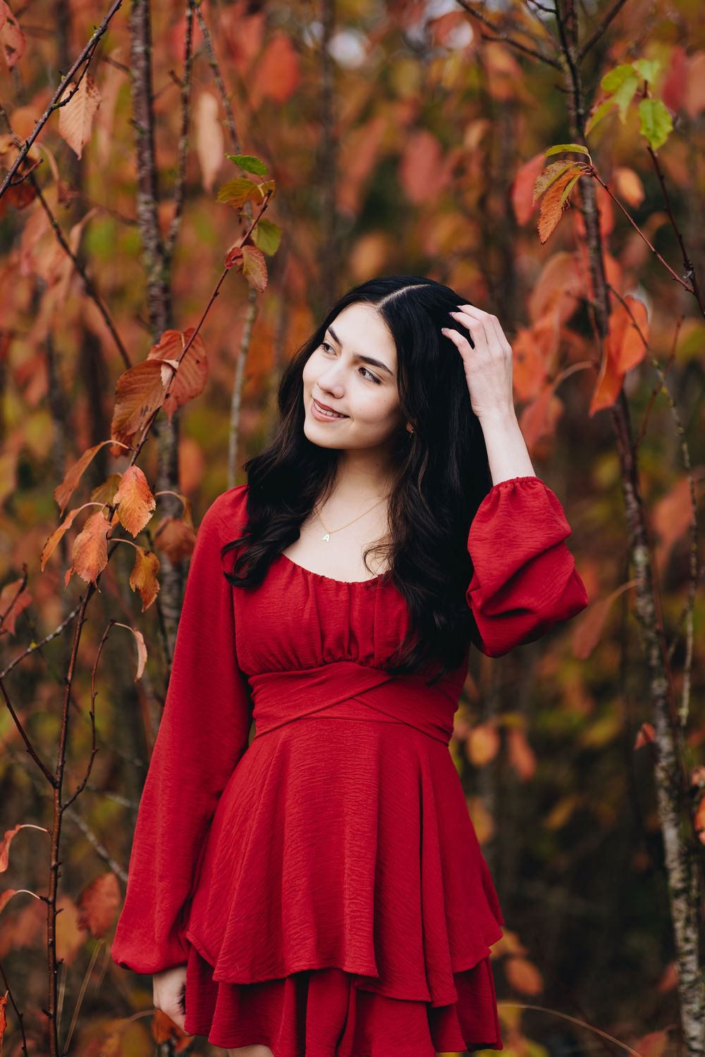 Portrait in red dress against autumn foliage with vibrant orange and red leaves.