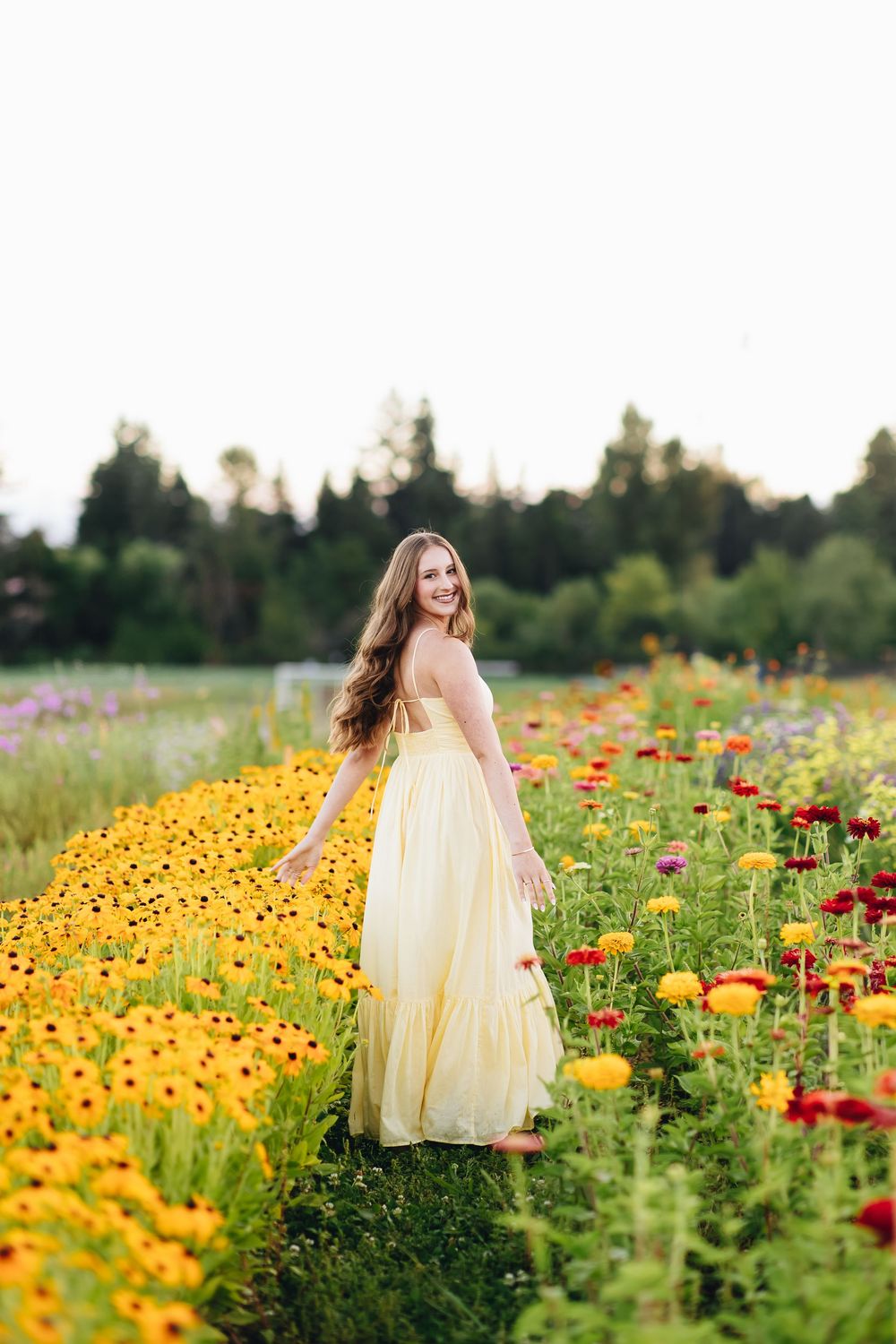 A person in a flowing yellow dress walks through a vibrant field of sunflowers and red poppies on a summer morning.