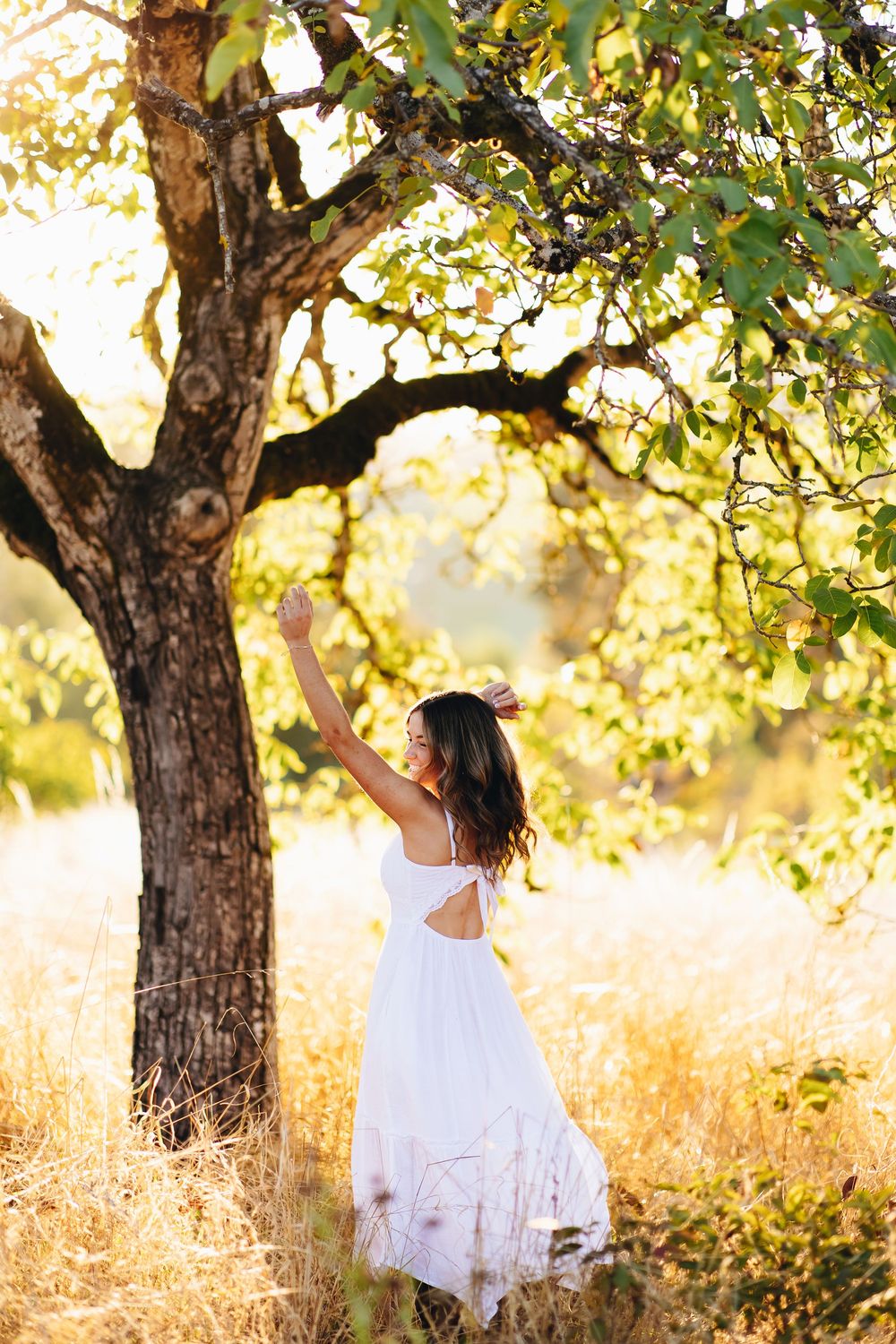 Ethereal portrait session in white dress under sun-dappled tree branches.