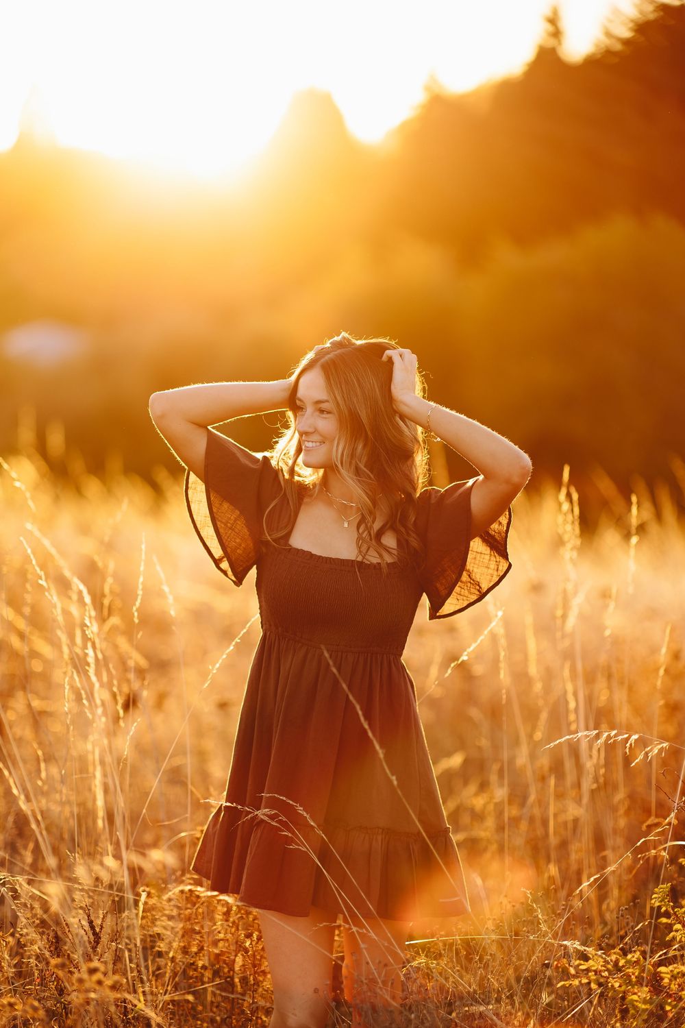 Dreamy golden hour portrait in black dress amid tall grass at sunset.