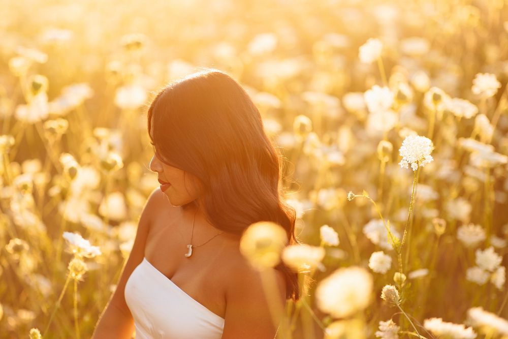 A girl in a sunlit field of tall grass and wildflowers during golden hour.