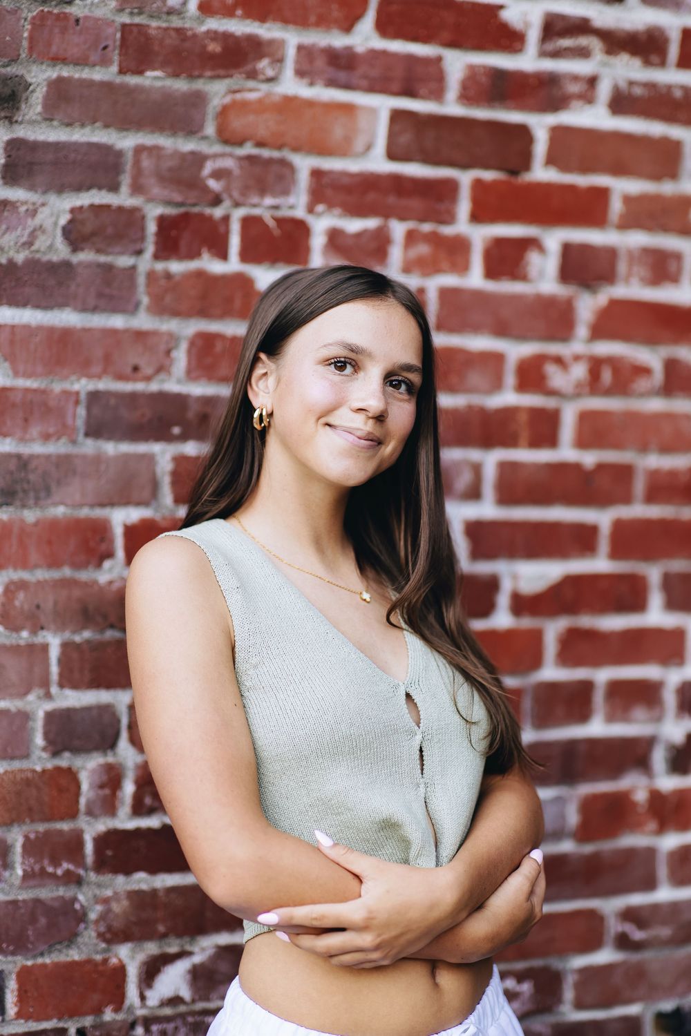 A young woman in a light green top poses against a rustic red brick wall in a series of portrait shots.