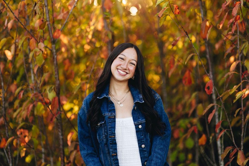 Autumn portrait session with colorful fall foliage and golden lighting in background.