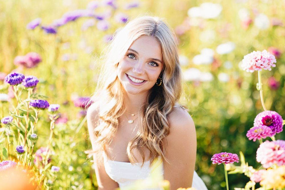 A person poses in a field of colorful wildflowers during golden hour with soft sunlight illuminating the scene.