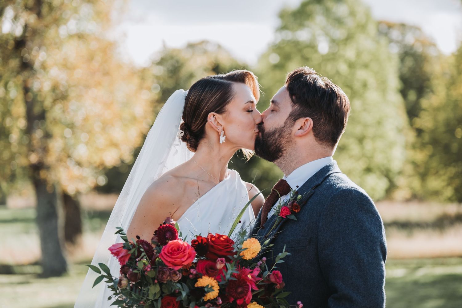 Bride and groom sharing a kiss with a vibrant red and orange wedding bouquet.