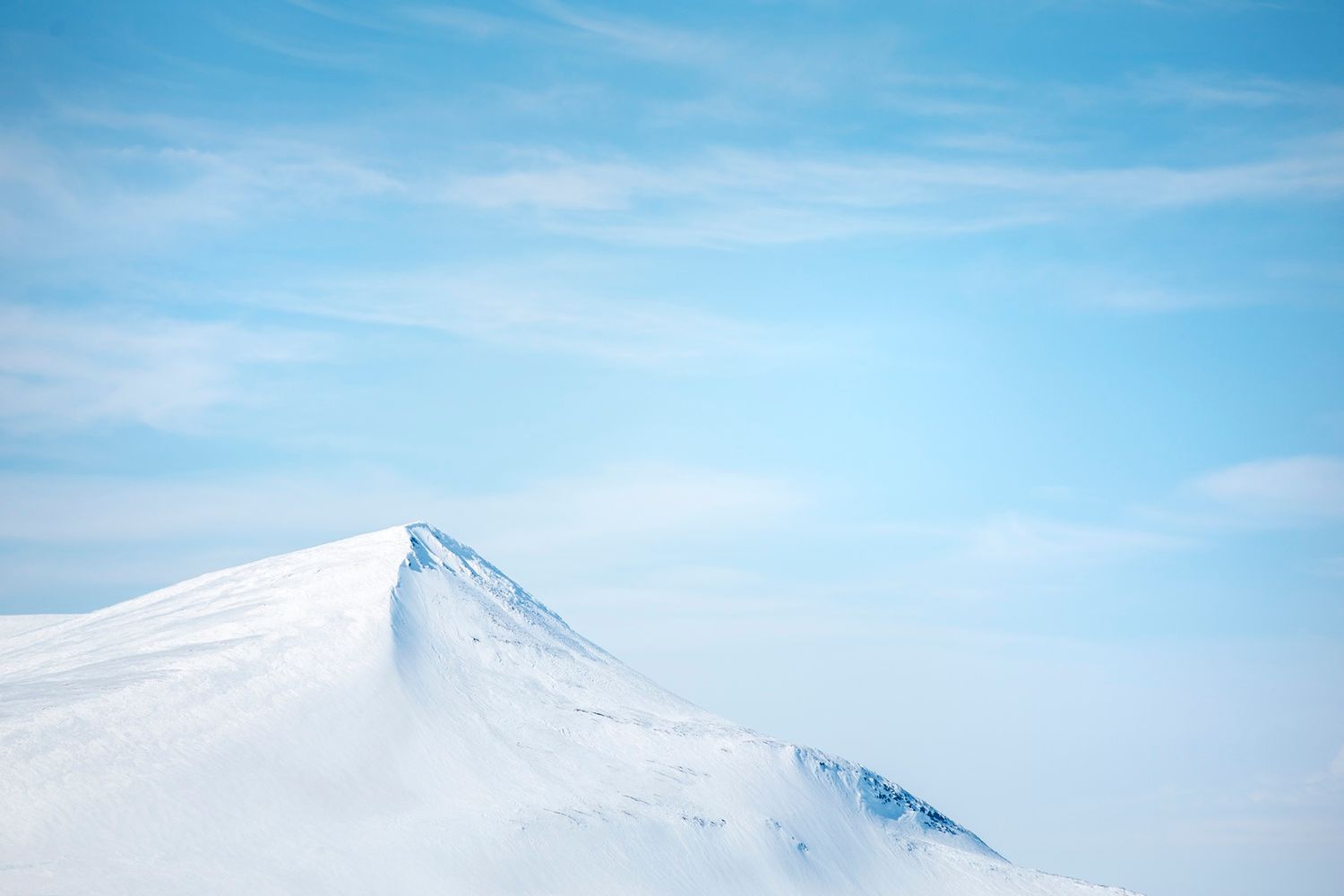 Minimalist snow-covered mountain peak rising against a pale blue sky in a serene Arctic landscape.