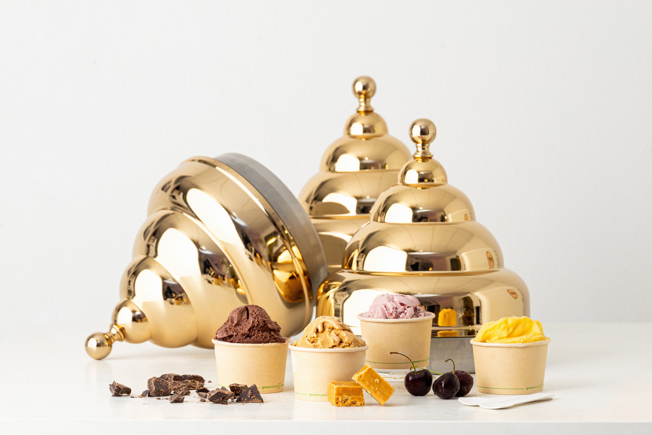 Three golden dome-shaped cloche covers displayed alongside small dishes containing colorful ingredients and garnishes.
