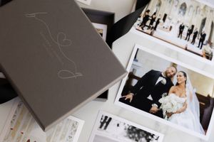 A wedding photo album with prints scattered on surface showing elegant gray cover and black and white photographs.