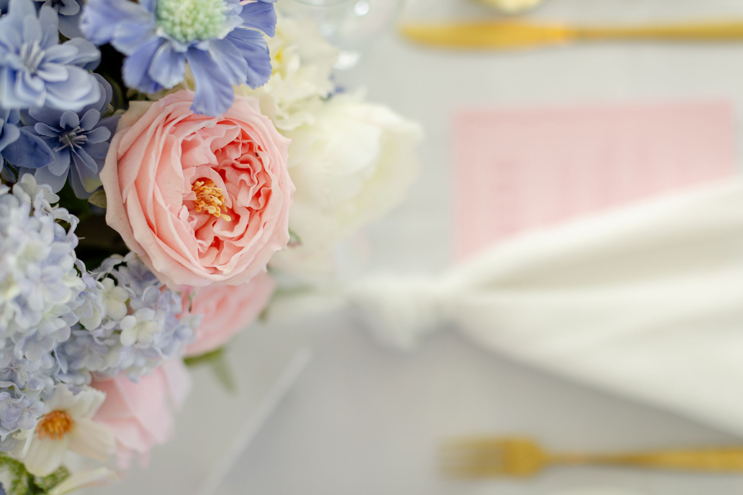 A soft pink garden rose and blue delphinium flowers in a romantic wedding bouquet with dreamy blurred background.