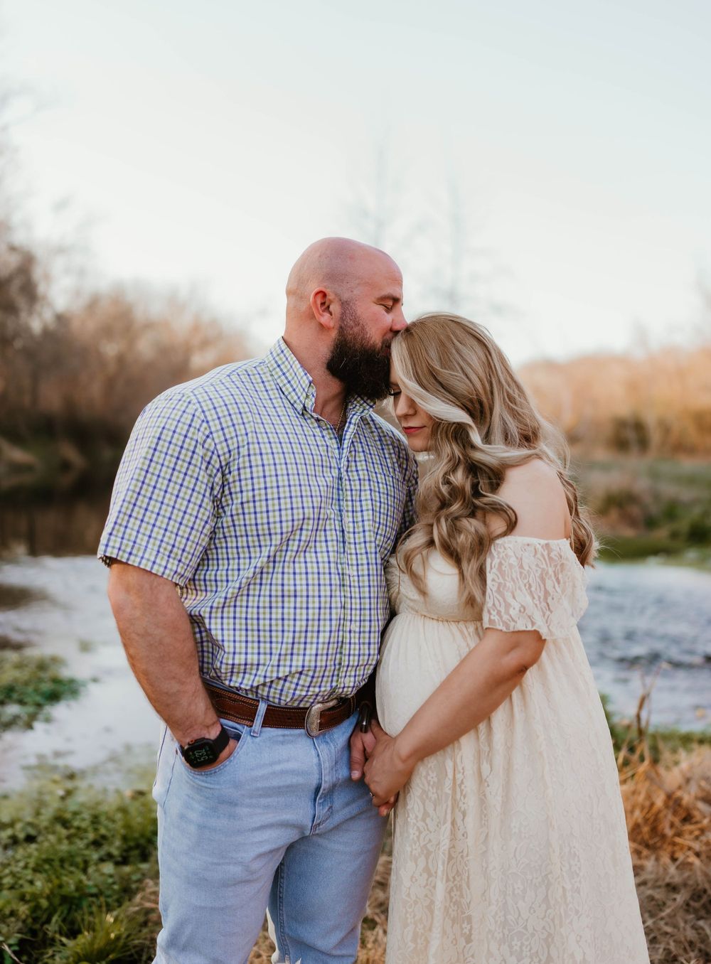 Couple in casual attire sharing intimate moment by river.