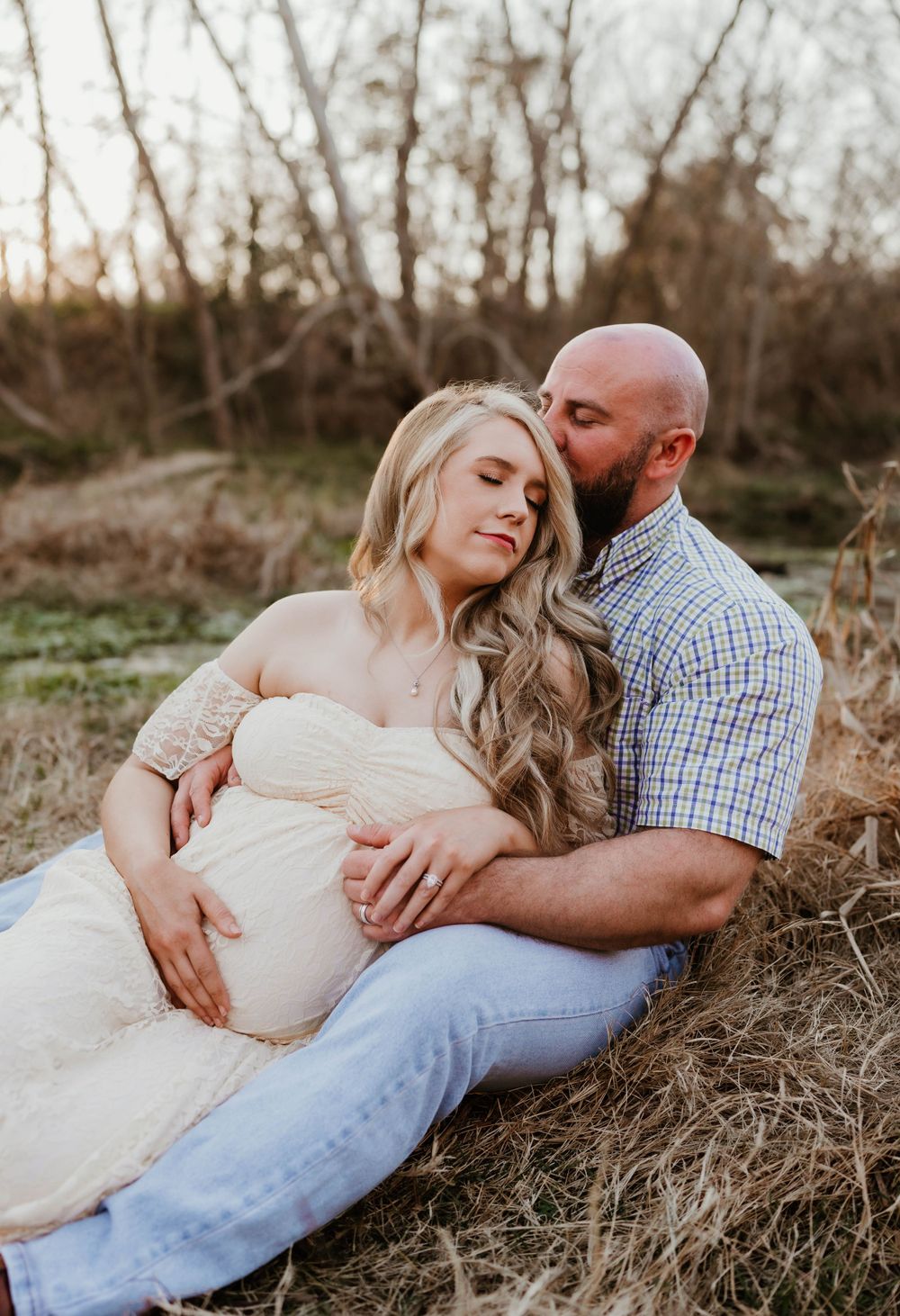A tender maternity photoshoot in a natural setting at sunset with a couple resting in golden grass.