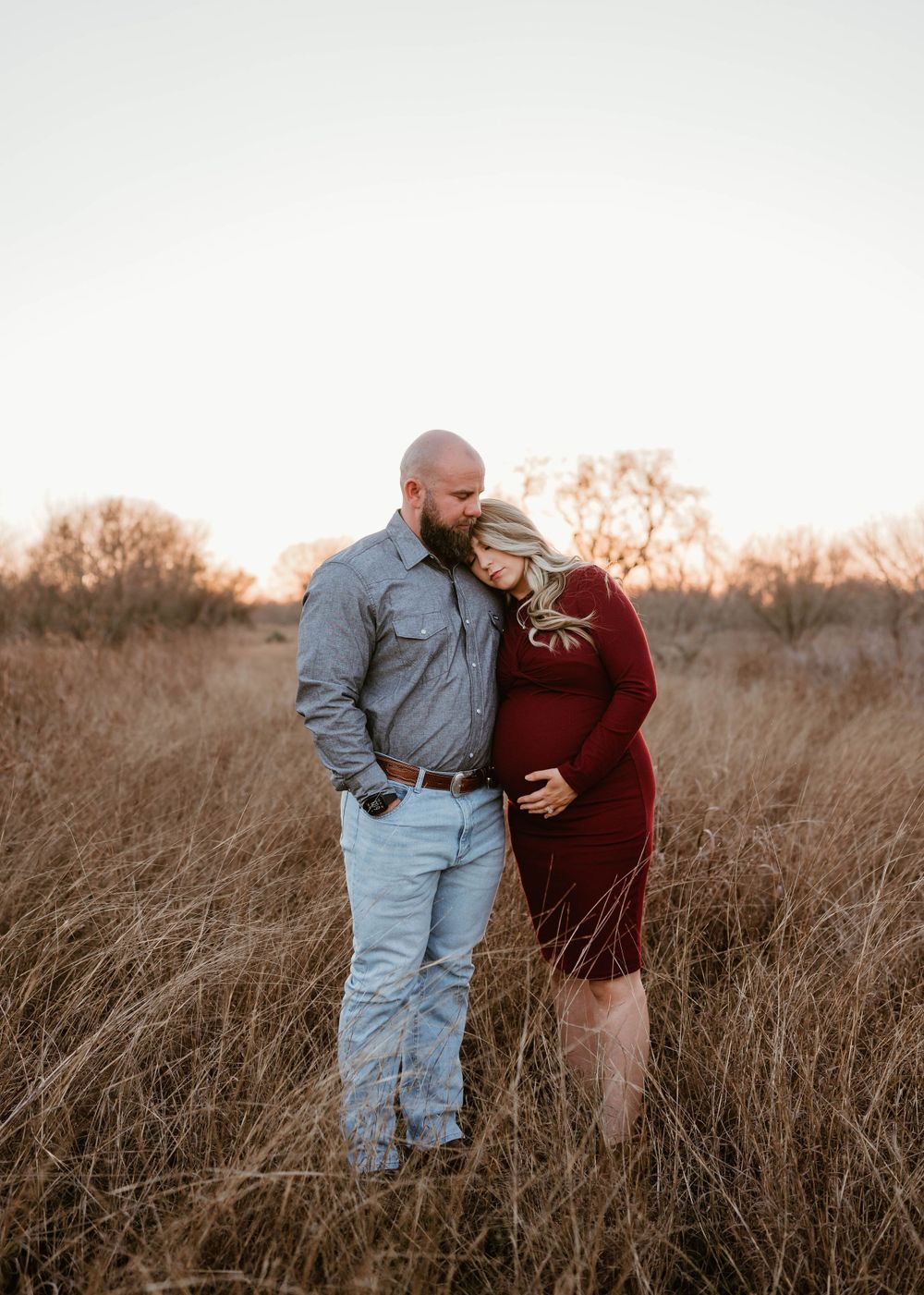 Intimate maternity photo of a couple embracing in tall autumn grass at sunset.