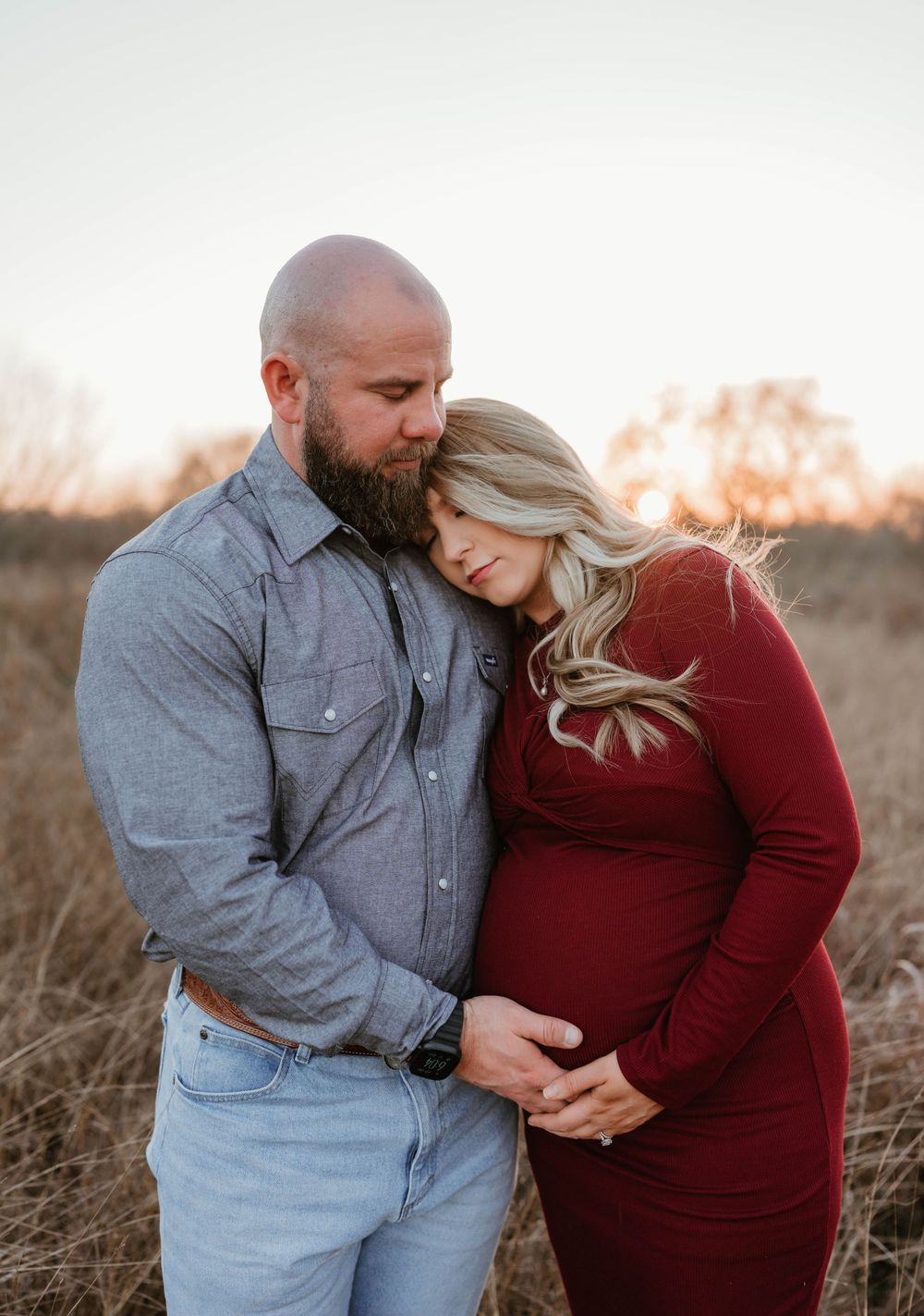 Romantic maternity moment captured in a field during golden hour.