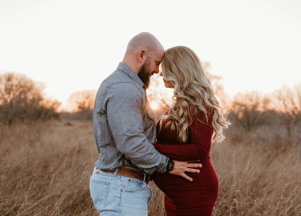 Intimate maternity portrait in a golden field with soft sunset lighting.