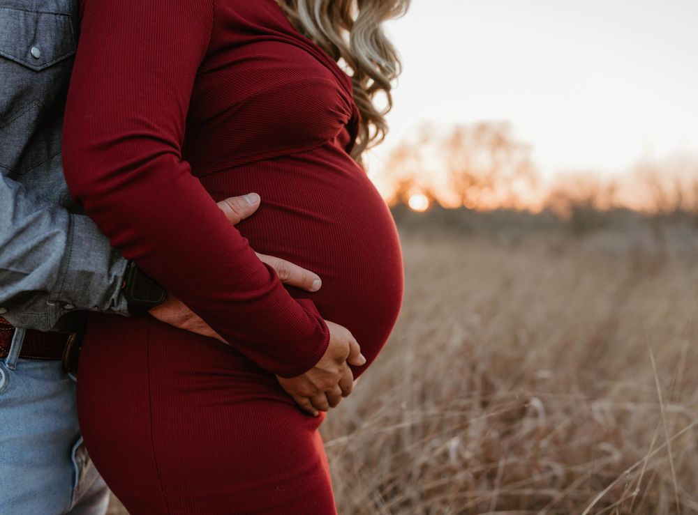 Close-up maternity photo showing hands cradling baby bump in burgundy dress.