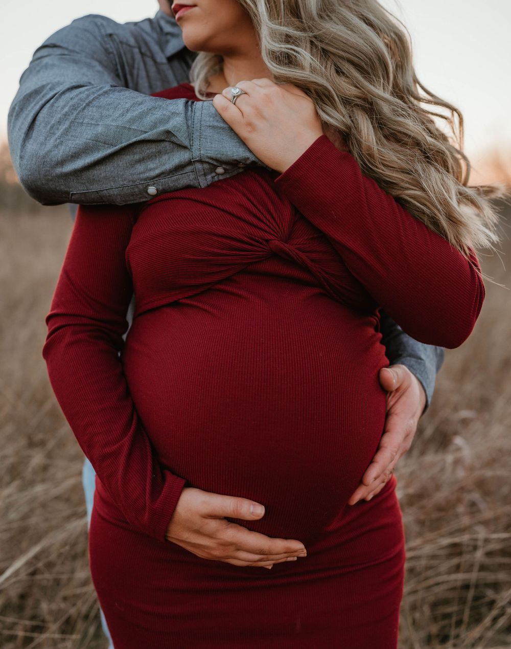 Intimate close-up of expectant parents embracing in burgundy maternity dress.