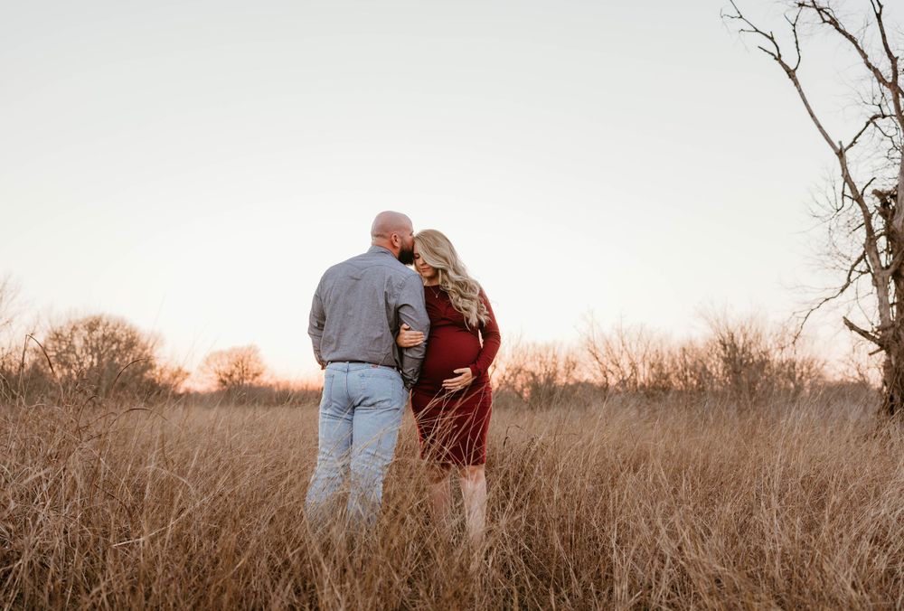 Silhouetted couple sharing intimate moment in field during sunset maternity shoot.