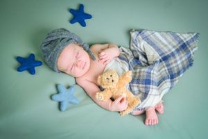 Sleeping newborn with teddy bear surrounded by blue star decorations on mint green background.