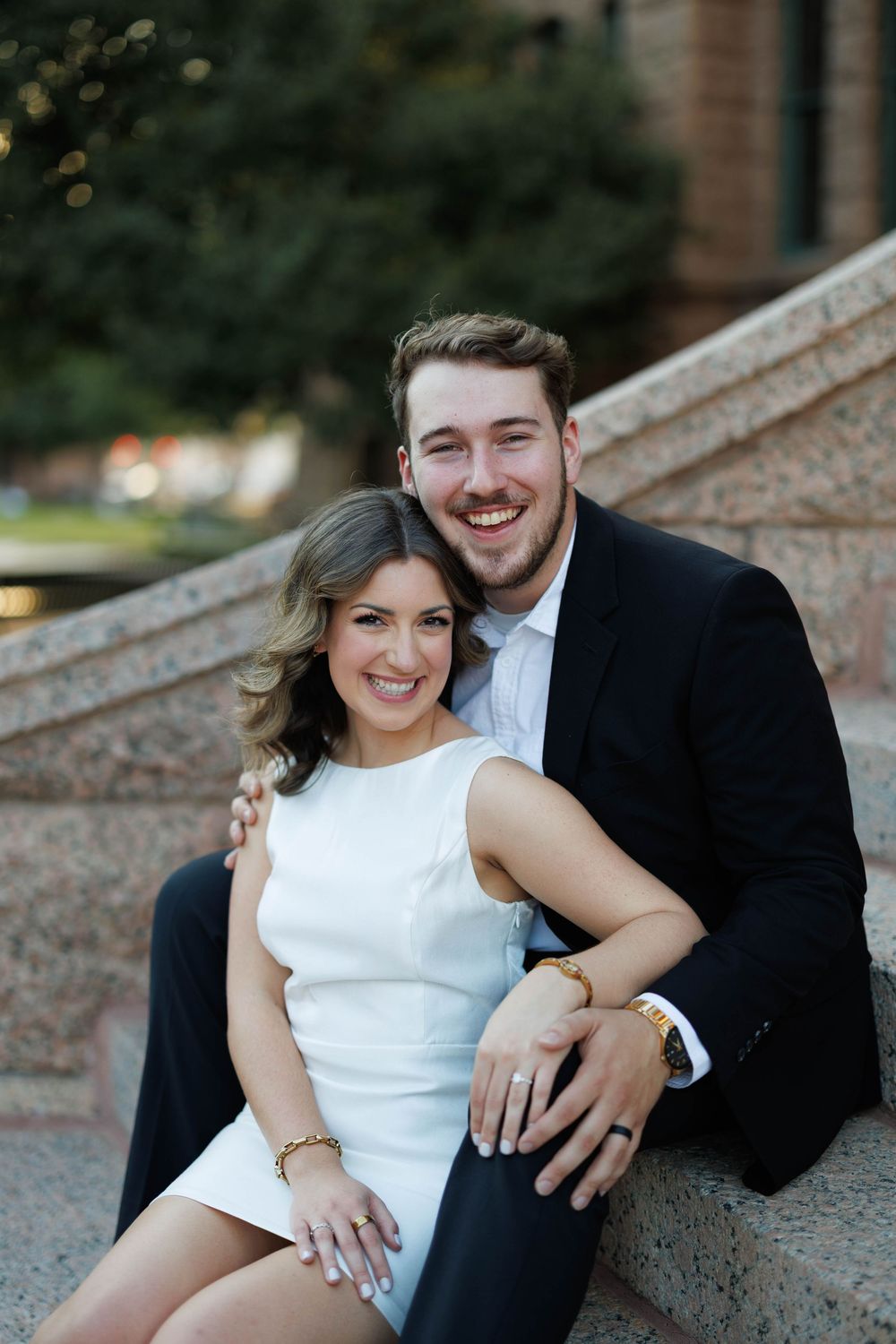 Smiling couple sitting together on granite steps of a historic building, woman in white dress.