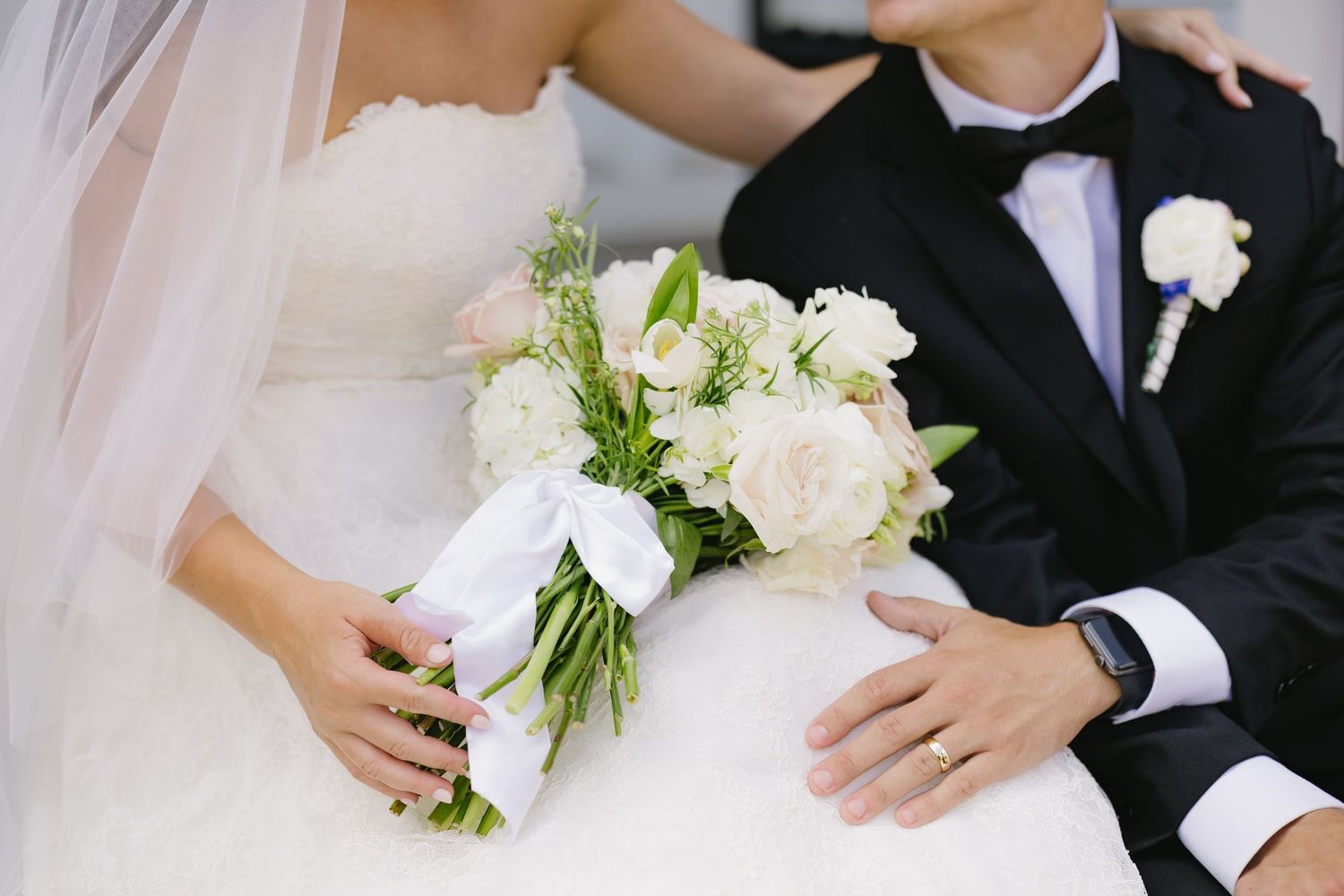 Close-up of bride and groom sitting together with elegant white and blush wedding bouquet.