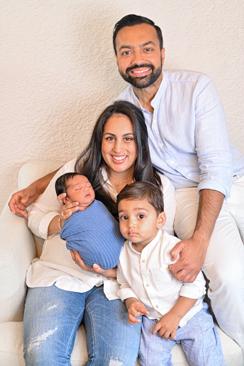 A family of four poses together against a white wall for a casual portrait.