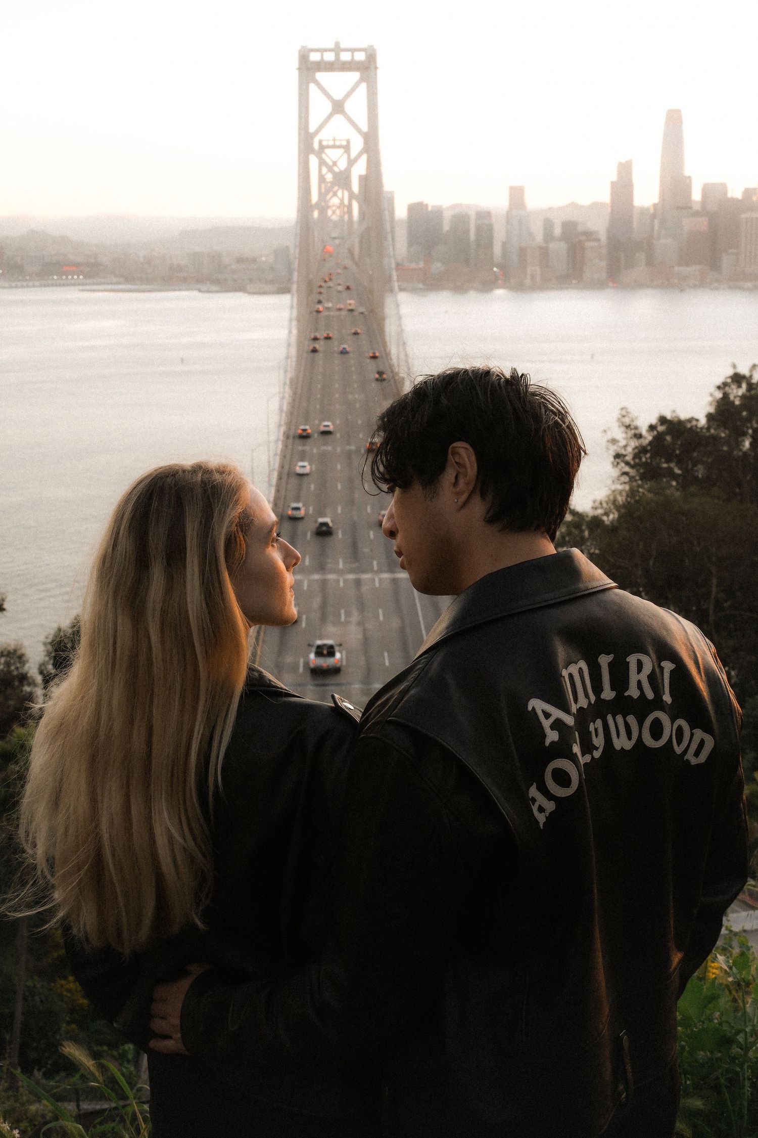 Romantic couple embracing on beach with Golden Gate Bridge visible in background.