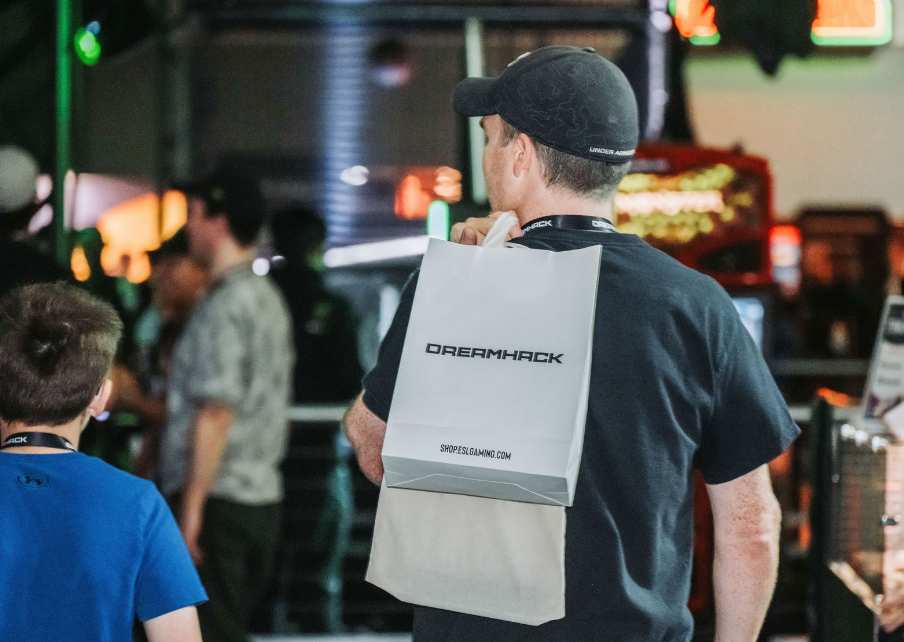 Person wearing a baseball cap carries a DoorDash package in a dimly lit indoor setting.