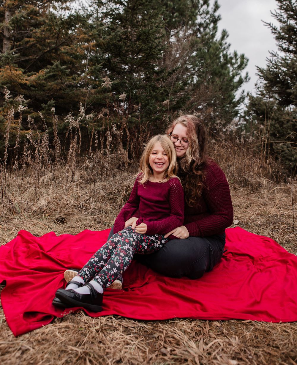 Two people share intimate moments on a red blanket in a rustic outdoor setting during autumn.