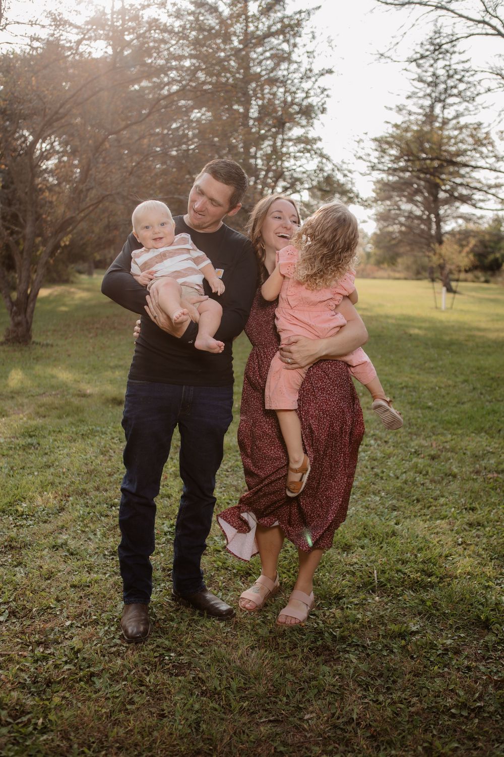 A family plays together in a sunlit field during golden hour with trees in the background.