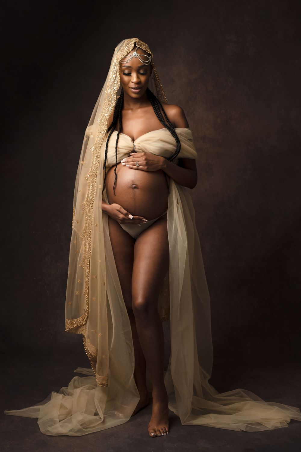 Artistic maternity photo series showing an expectant mother draped in golden sheer fabric against dark background.