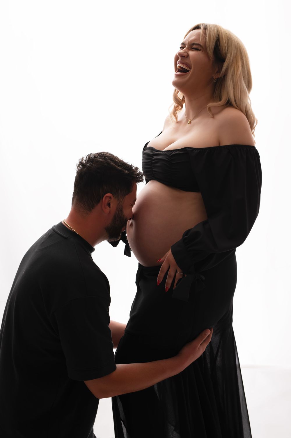 Maternity photo series showing intimate moments between expecting couple in black attire against white backdrop.