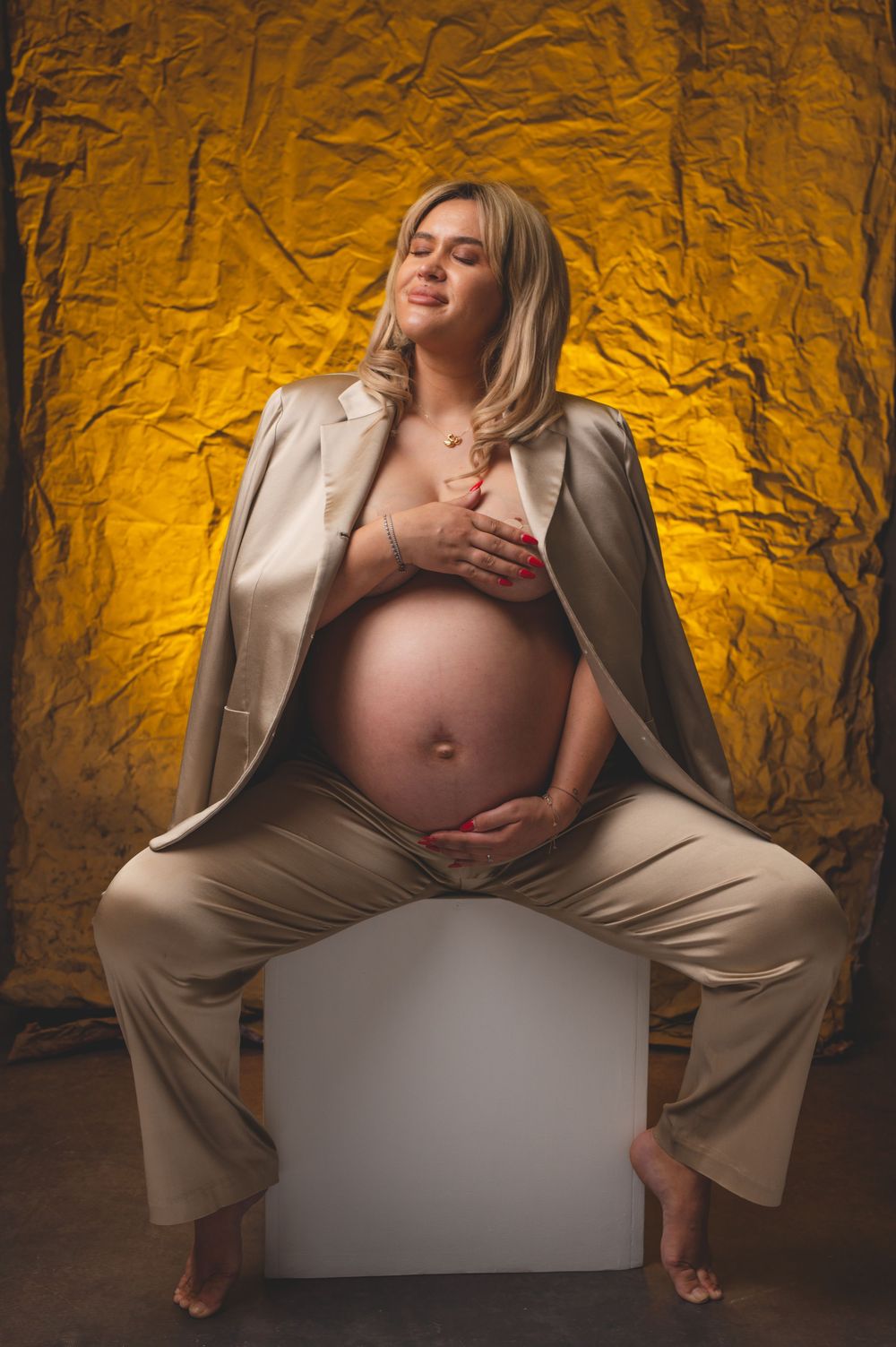Dramatic maternity portraits with golden lighting against textured wall backdrop.