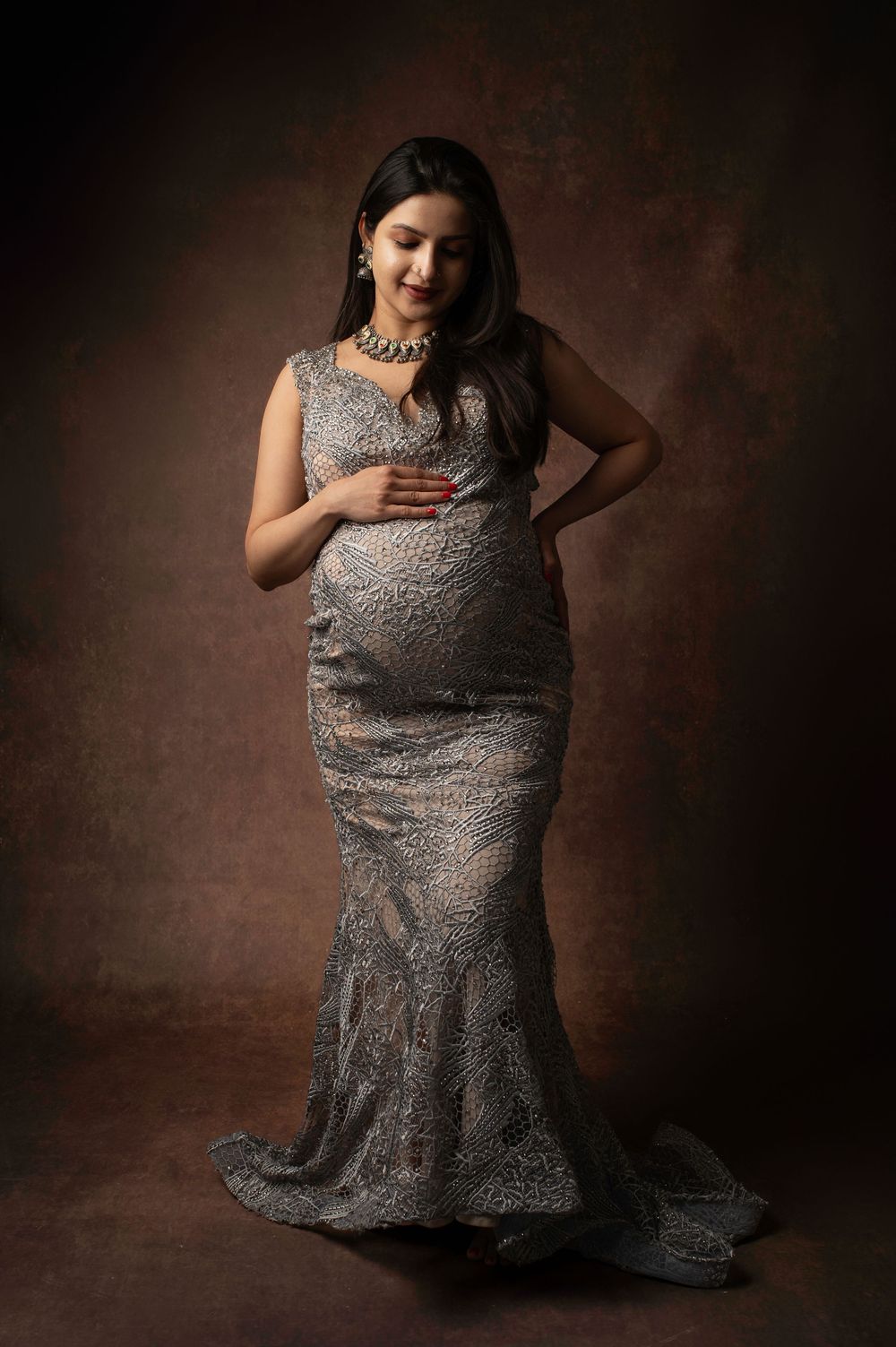 A person poses gracefully in a silver sequined evening gown against a dark brown studio backdrop.