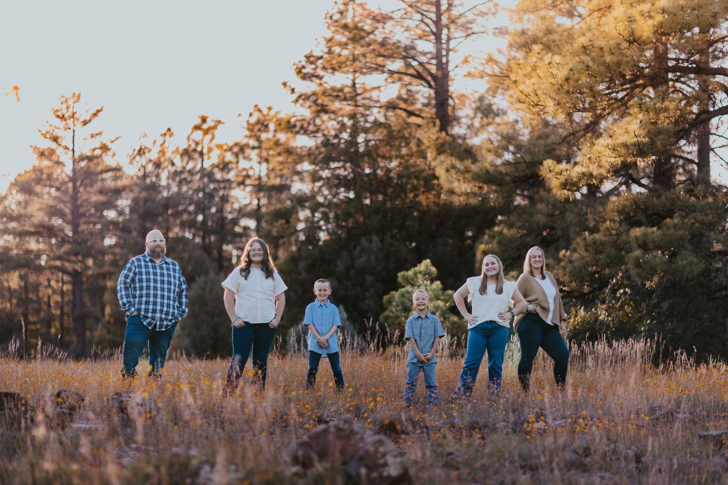 Family walking together through tall grass field during golden hour.