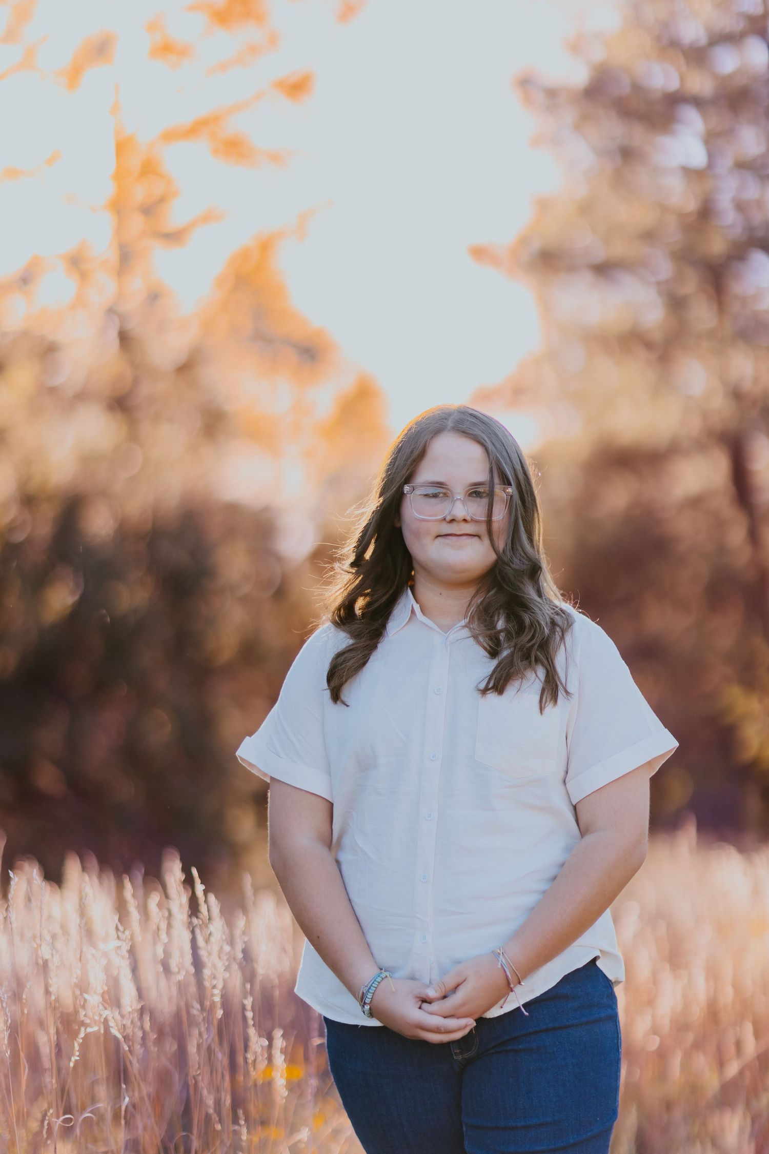 Portrait session in a golden field during sunset wearing white top and blue jeans.