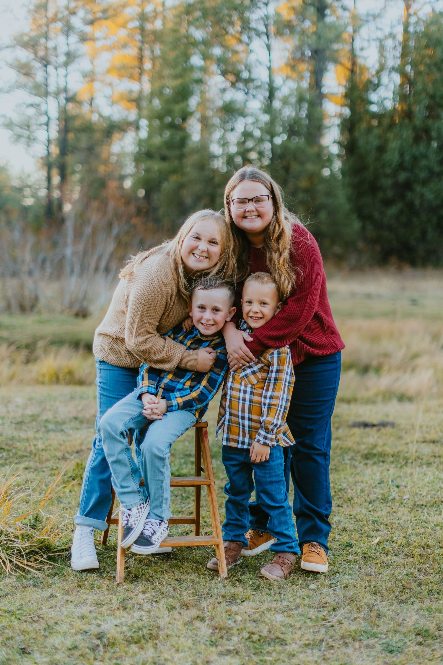 A casual outdoor family portrait with a wooden stool against an autumn forest backdrop.