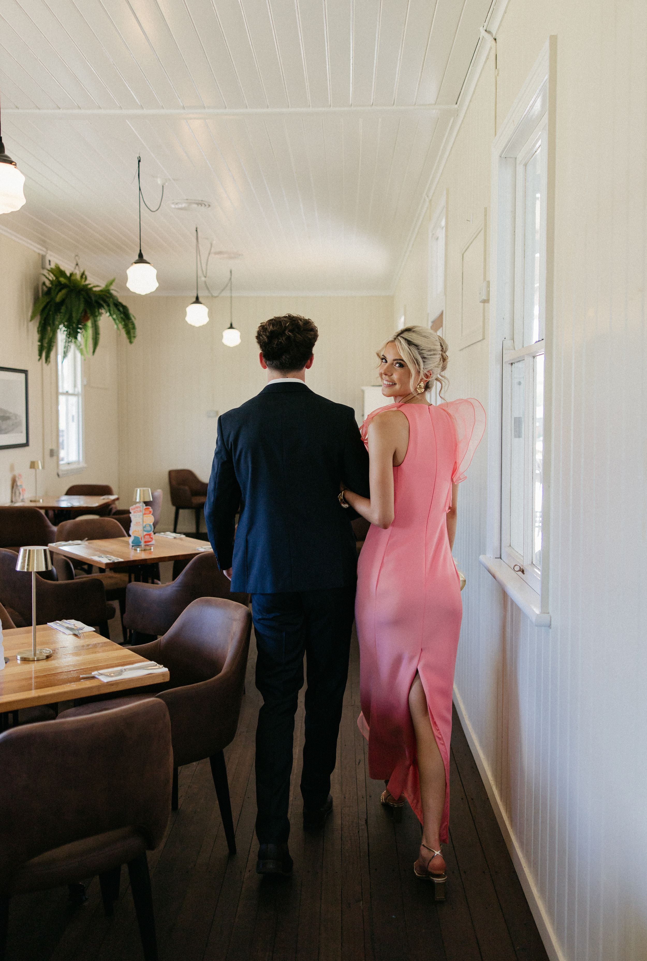 Couple walking through elegant restaurant, woman in pink slit dress, man in navy suit.