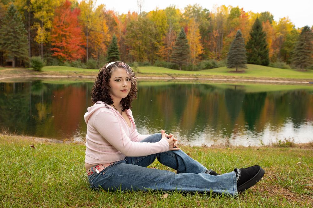 Person relaxing by a serene autumn lake surrounded by vibrant fall foliage and colorful trees.