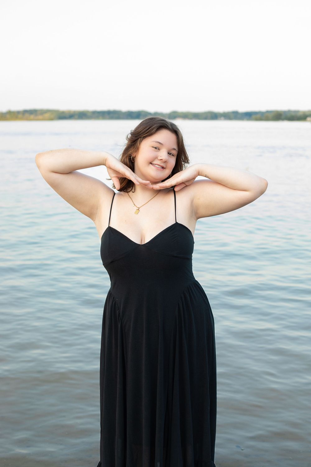 Woman in black dress stretches by water during outdoor photoshoot sequence.