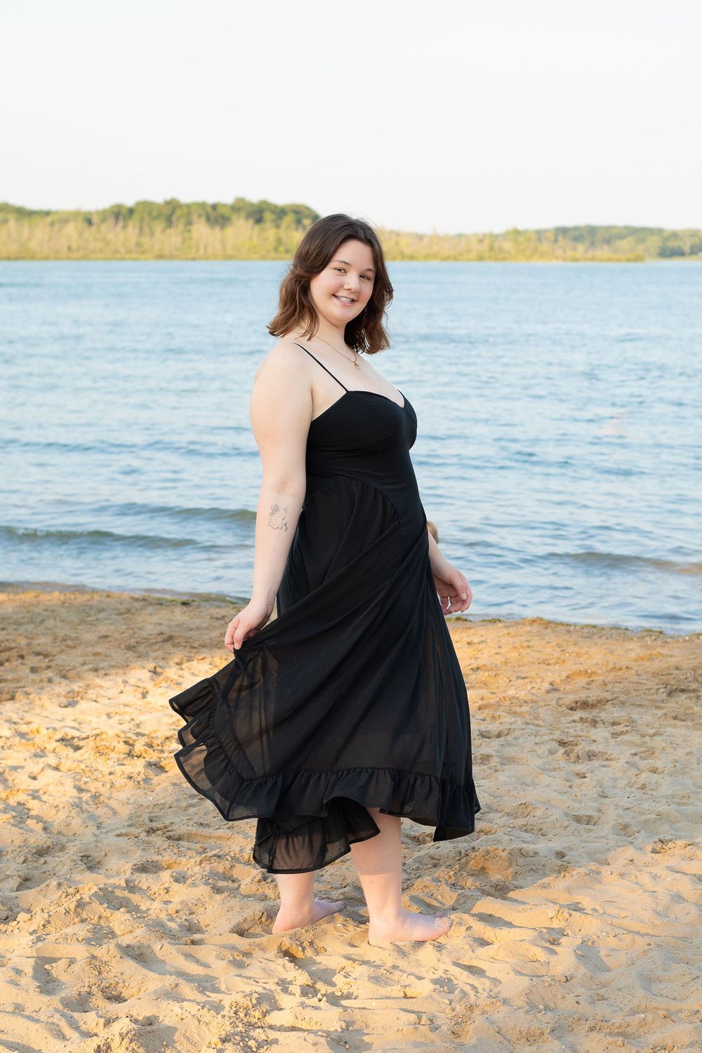 A carefree figure in a flowing black dress twirls on a sunny beach beside blue waters, creating a joyful scene.
