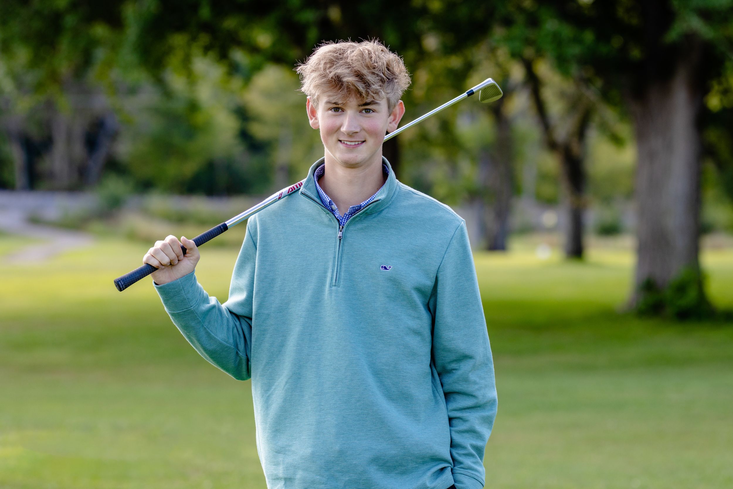 Person in light blue sweater holding a golf club on a green course.