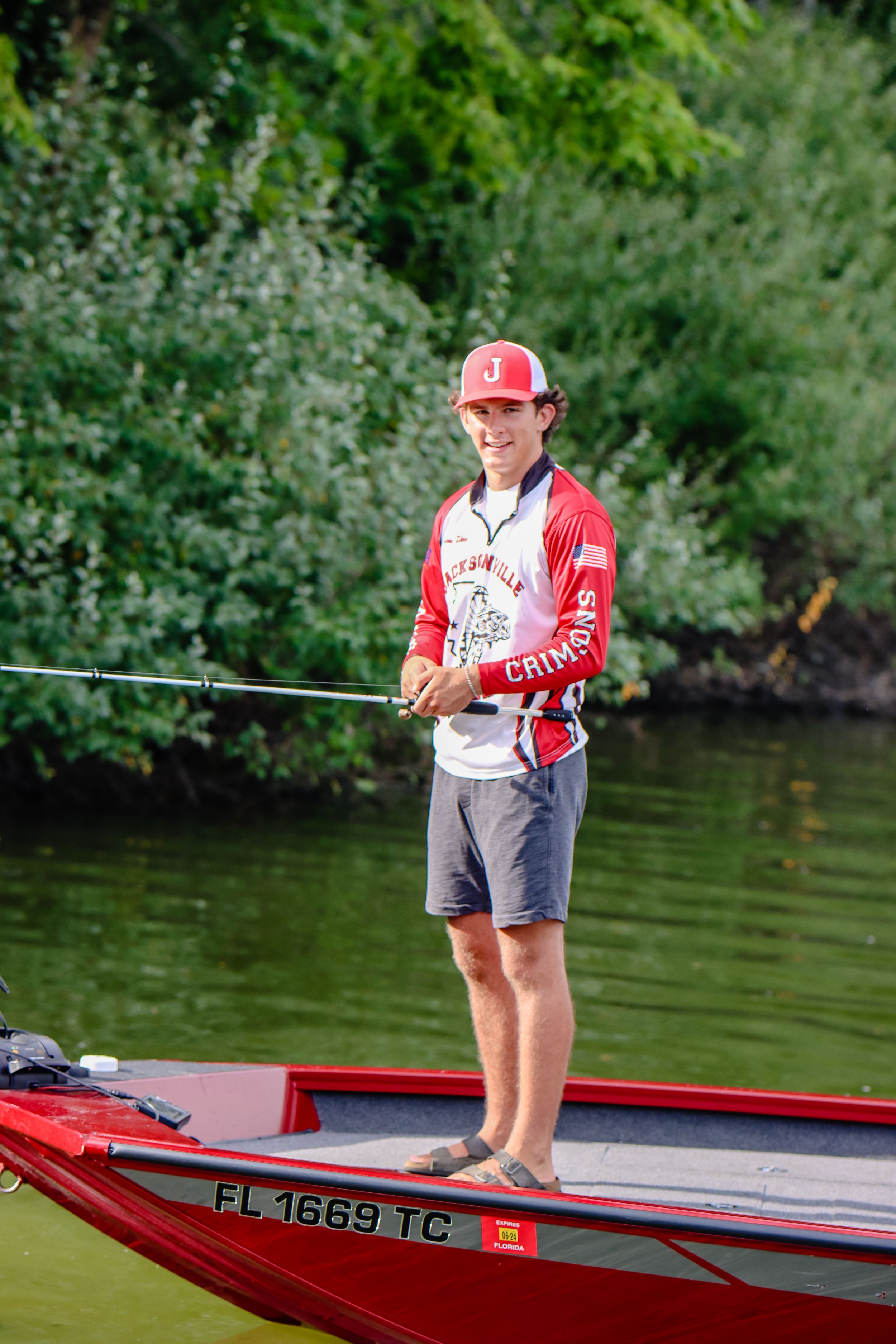 A fisherman in red and white gear stands on a boat deck with fishing rod.