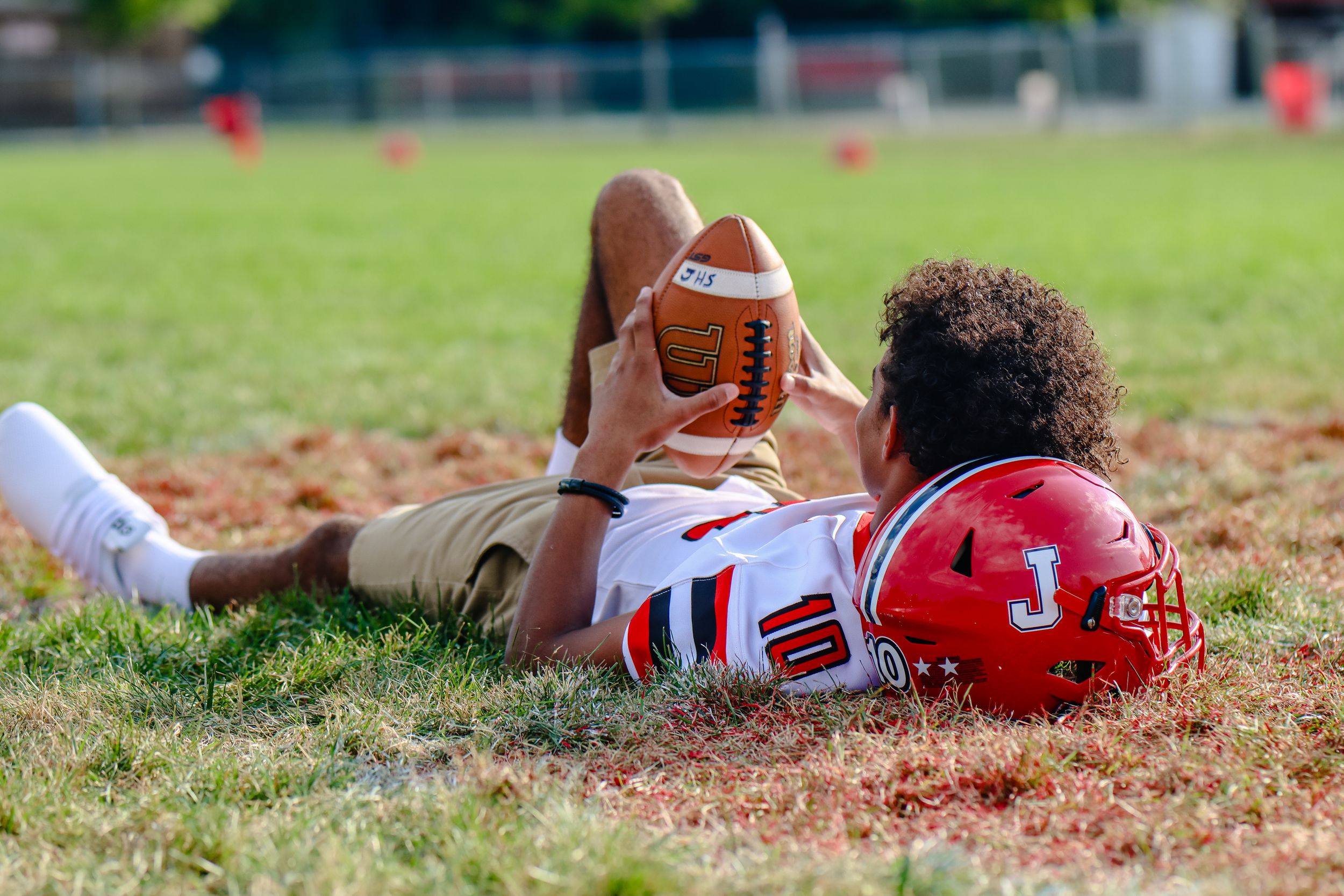 Athletes resting on grass field with sports equipment during practice.
