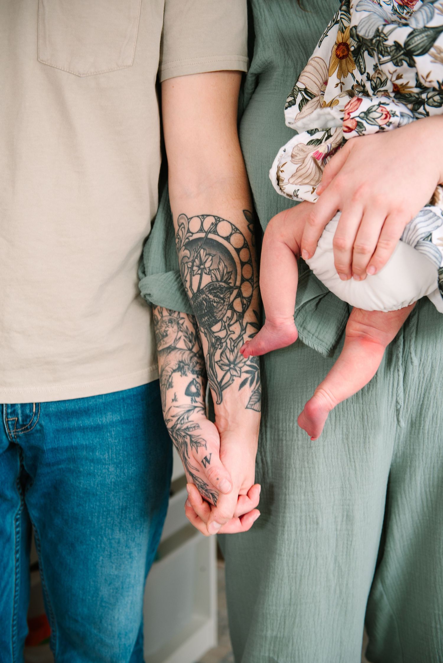 Close-up of tattooed arms holding hands showing detailed floral ink artwork.