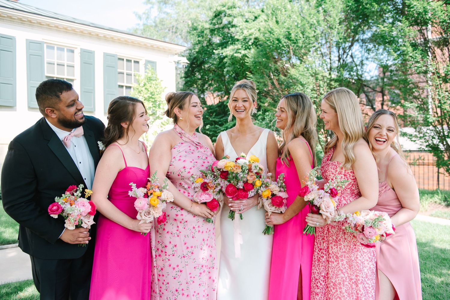 Wedding party in bright pink and floral dresses smiling together outdoors on sunny day.