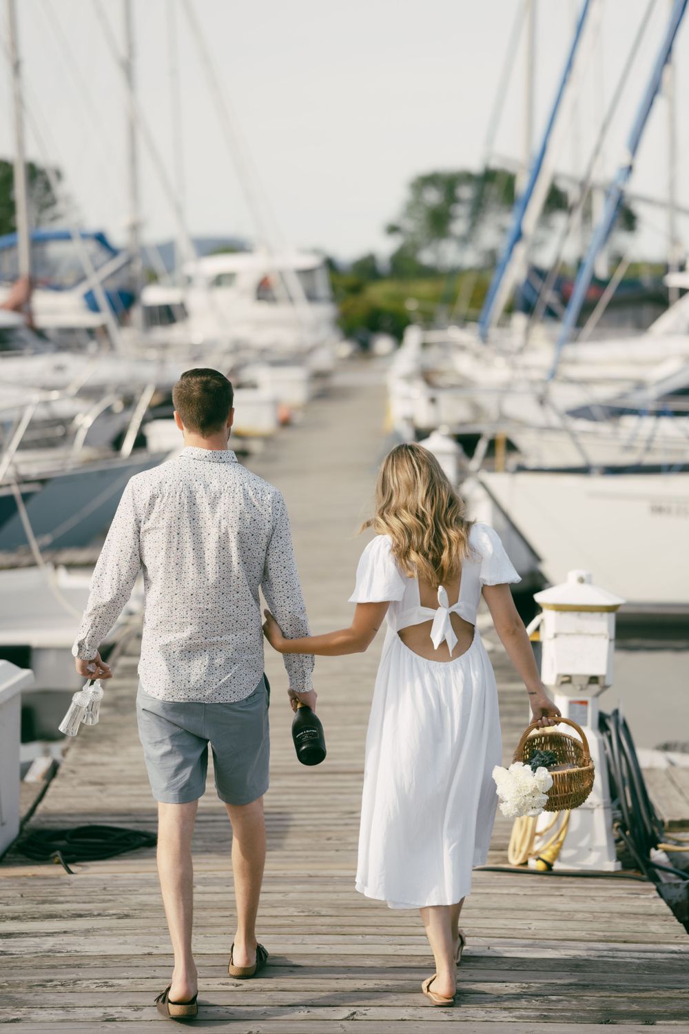 Couple walking together on a wooden dock at a marina with boats in the background.