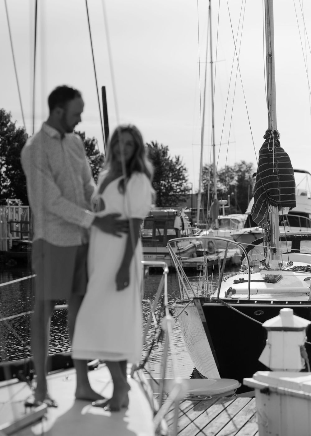 A romantic couple shares a tender moment on a sailboat dock at sunset with boats in the marina.